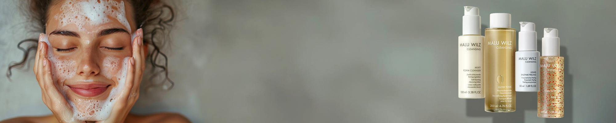 Nahaufnahme einer Frau mit geschlossenen Augen, Reinigungsschaum im Gesicht, beide Hände auf den Wangen, vor grauem Hintergrund, daneben die MALU WILZ Cleansing Produktgruppe.
