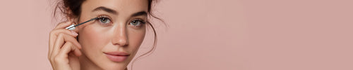 Close-up Gesicht Frau, die Mascara in der Hand hält und auf Wimpern aufträgt vor rosa Hintergrund