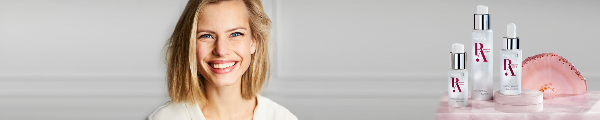 Nahaufnahme einer blonden Frau vor weißer Wand; seitlich die MALU WILZ Premium Aging Produktgruppe.