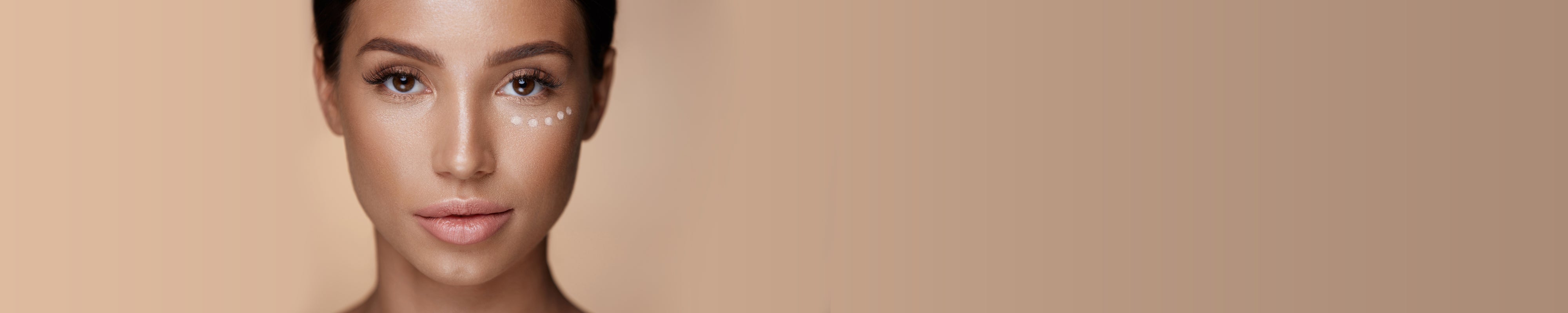 Gesicht Frau mit Concealer Punkten unter dem Auge sowie Textur an der Seite vor braunem Hintergrund