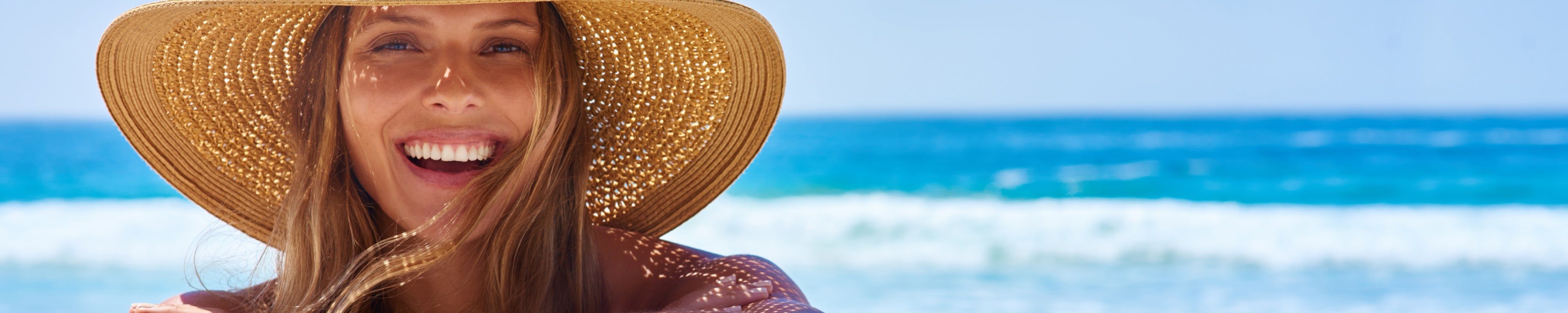 Gesicht lachende Frau mit Sonnenhut und im Hintergrund Meer