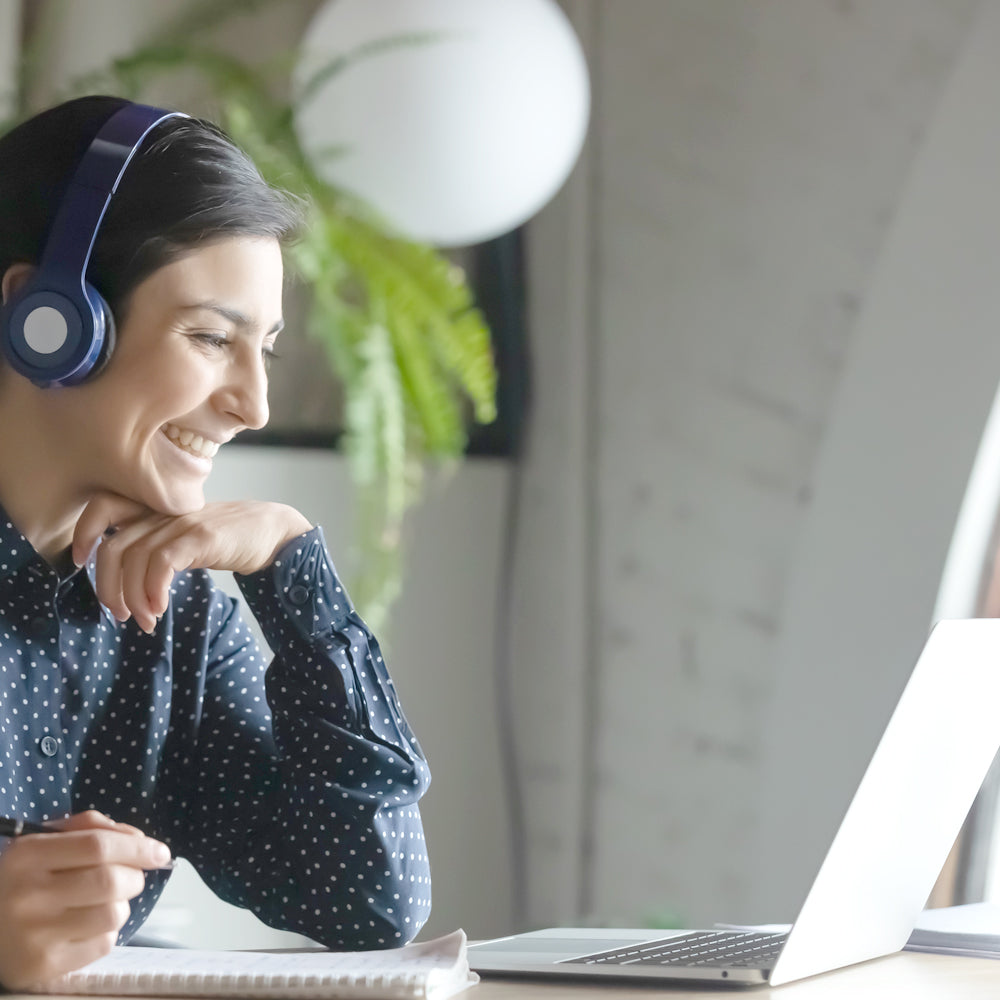 Eine lächelnde Person mit Kopfhörern sitzt vor einem Laptop und nimmt an einer Videokonferenz oder einem Online-Training teil.