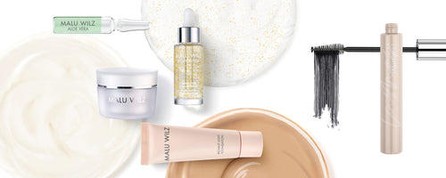 MALU WILZ Kosmetikprodukte: Auswahl aus Pflege und Make-up wie Foundation, Mascara, Serum und Gesichtscreme vor cremigen Texturen.