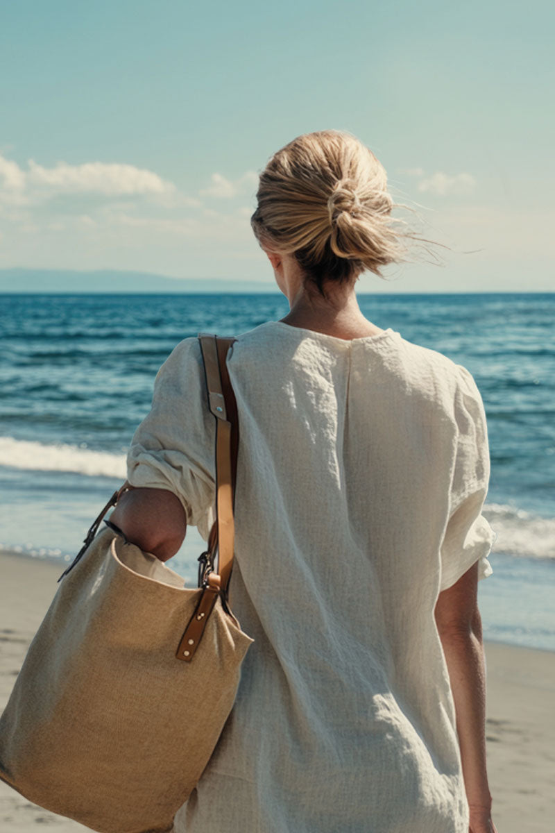 Frau am Strand mit großer Tasche über der Schulter, Rückansicht, Meer und blauer Himmel