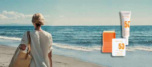 Frau am Strand mit großer Tasche über der Schulter, Rückansicht, Meer und blauer Himmel, Sun Care Produkte an der Seite