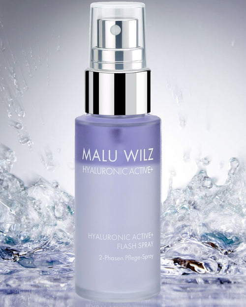 Malu Wilz Hyaluronic Active+ Flash Spray in einer violetten Sprühflasche vor einem Hintergrund mit spritzendem Wasser.