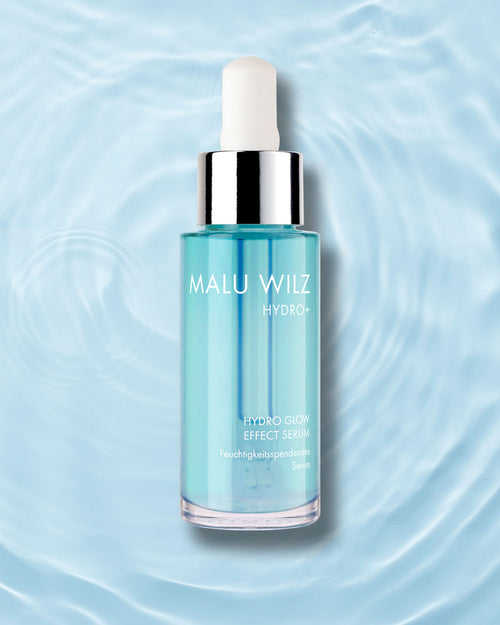 Malu Wilz Hydro+ Hydro Glow Effect Serum in einer blauen Pipettenflasche vor einem Hintergrund mit wasserähnlichen Wellen.