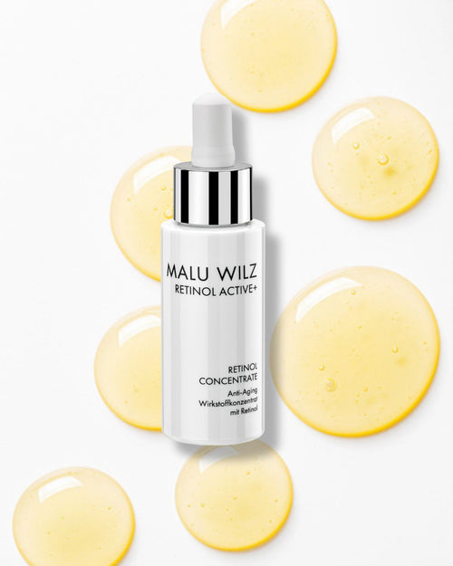 MALU WILZ Retinol Active+ Konzentrat: Anti-Aging-Wirkstoffkonzentrat in weißer Pipettenflasche vor gelben Produkt-Tropfen.