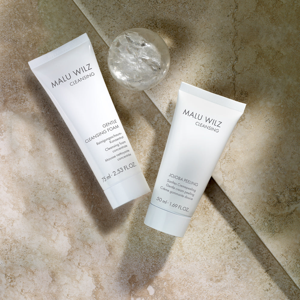 MALU WILZ Gentle Cleansing Foam und Jojoba Peeling mit Kristallkugel auf beigem Marmor-Hintergrund.