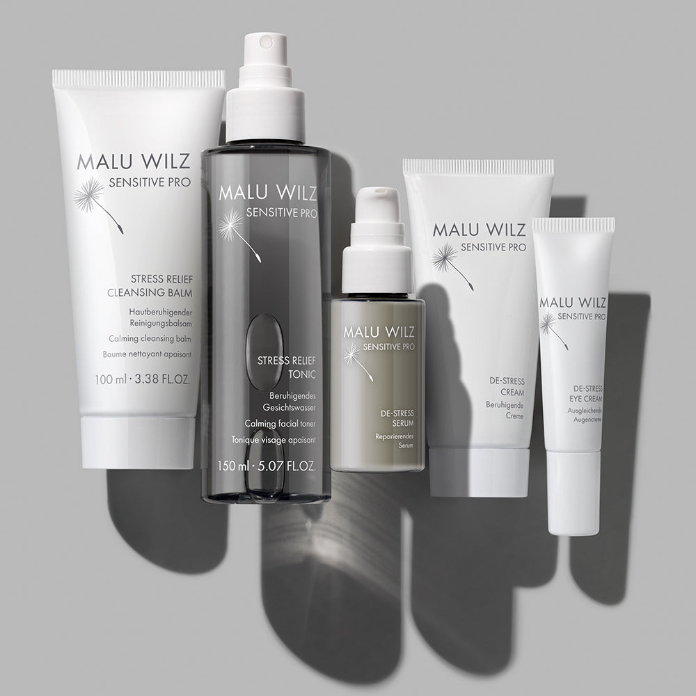 Eine Auswahl an Malu Wilz 'Sensitive Pro' Pflegeprodukten, darunter ein Reinigungsbalsam, ein Gesichtswasser, ein Serum, eine Creme und eine Augencreme.